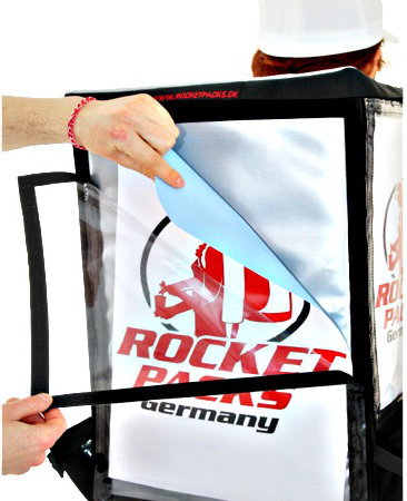 Close-up of a customizable advertising graphic being inserted into the transparent display panel of a RocketPacks TwinPack vending backpack.